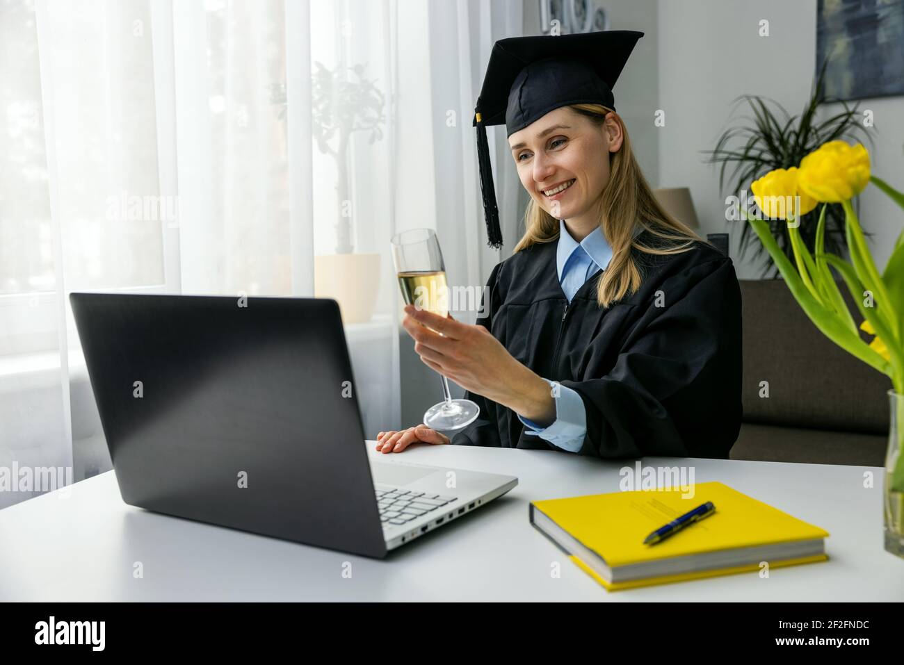 online graduation celebration - happy woman using laptop and drinking champagne together with university friends Stock Photo