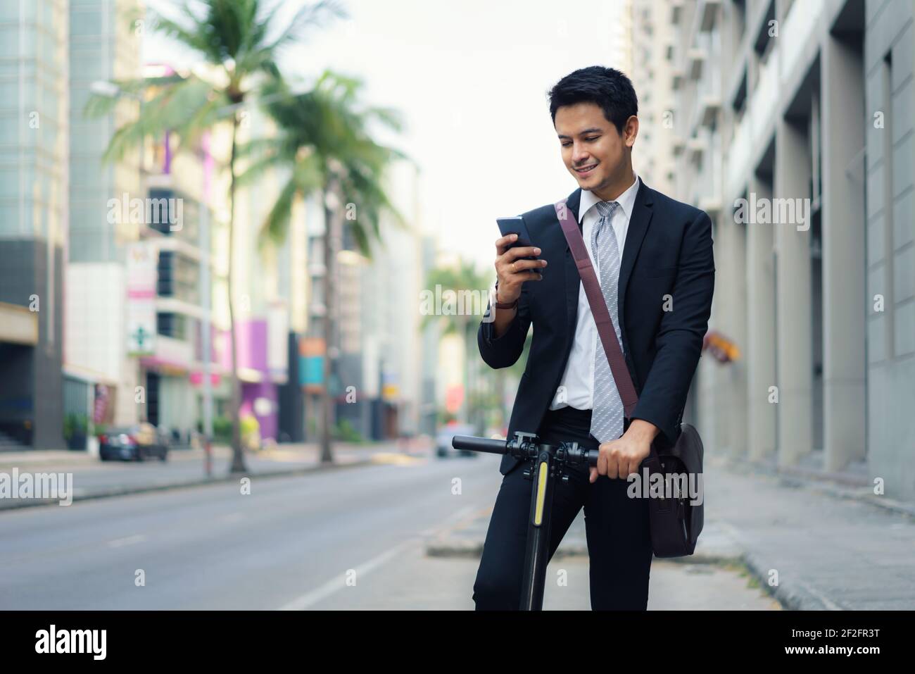 Asian businessman is riding an electric scooter and using his mobile phone to open a map in application to check the city road routes to work in the m Stock Photo
