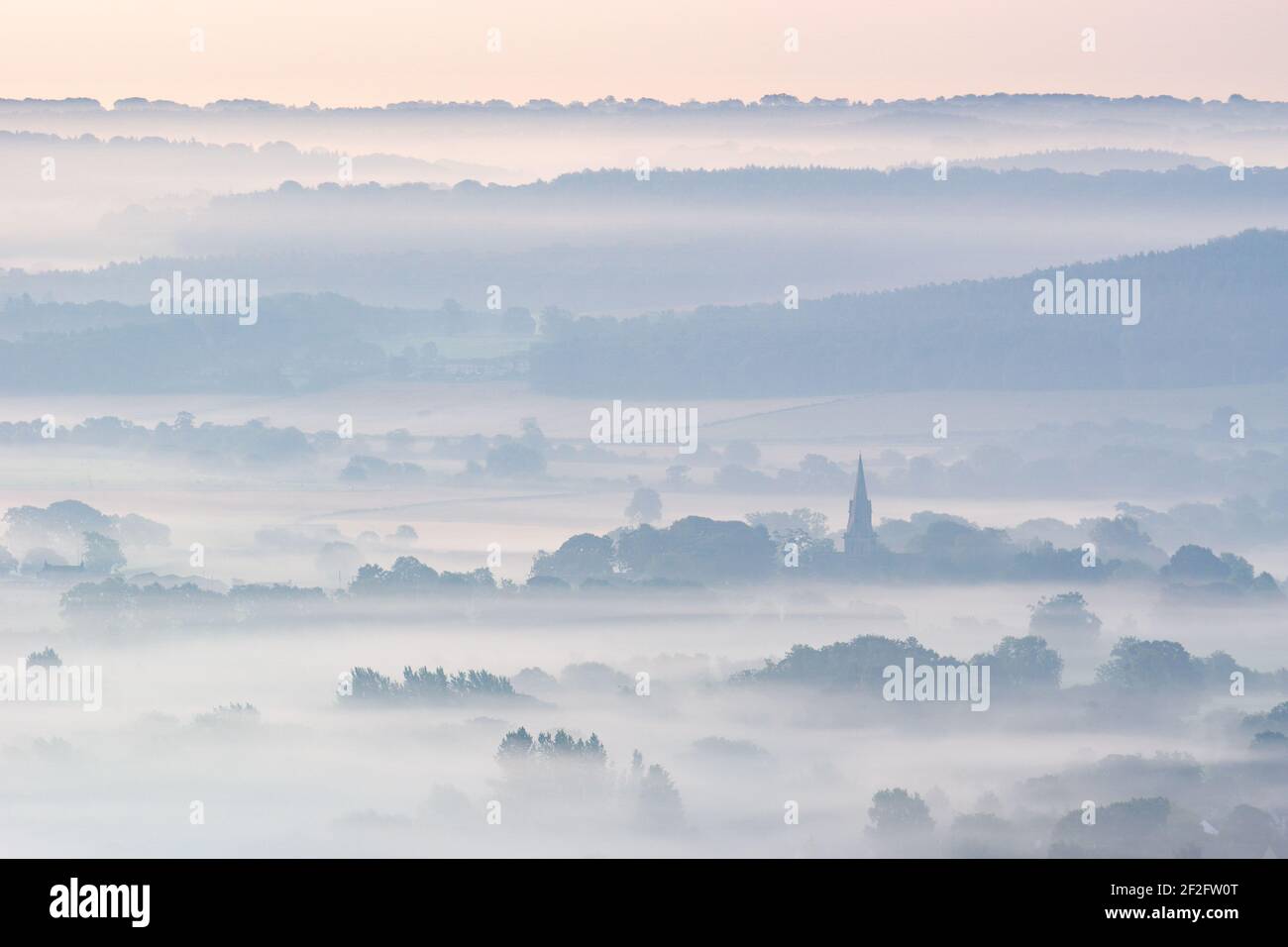 The spire of St Barnabas Church in Weeton, Yorkshire, is prominent above the misty layers of the landscape at dawn on a peaceful autumn morning. Stock Photo