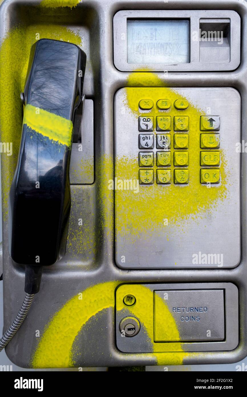 A detail of a public BT landline phone kiosk has been vandalised by the spraying of yellow aerosol paint over its handset and keypad on the Southbank in Waterloo, on 11th March 2021, in London, England. Stock Photo