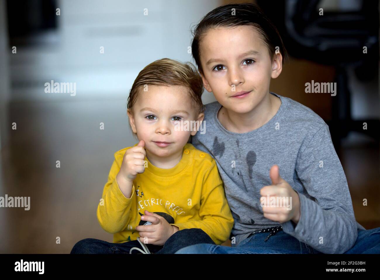 Two boys, brothers, showing thumbs up on the camera at home Stock Photo