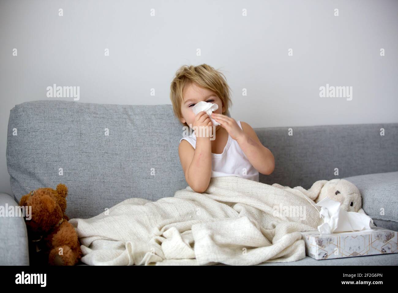 Blond toddler child, wiping his nose in a tissue, sneezing and coughing