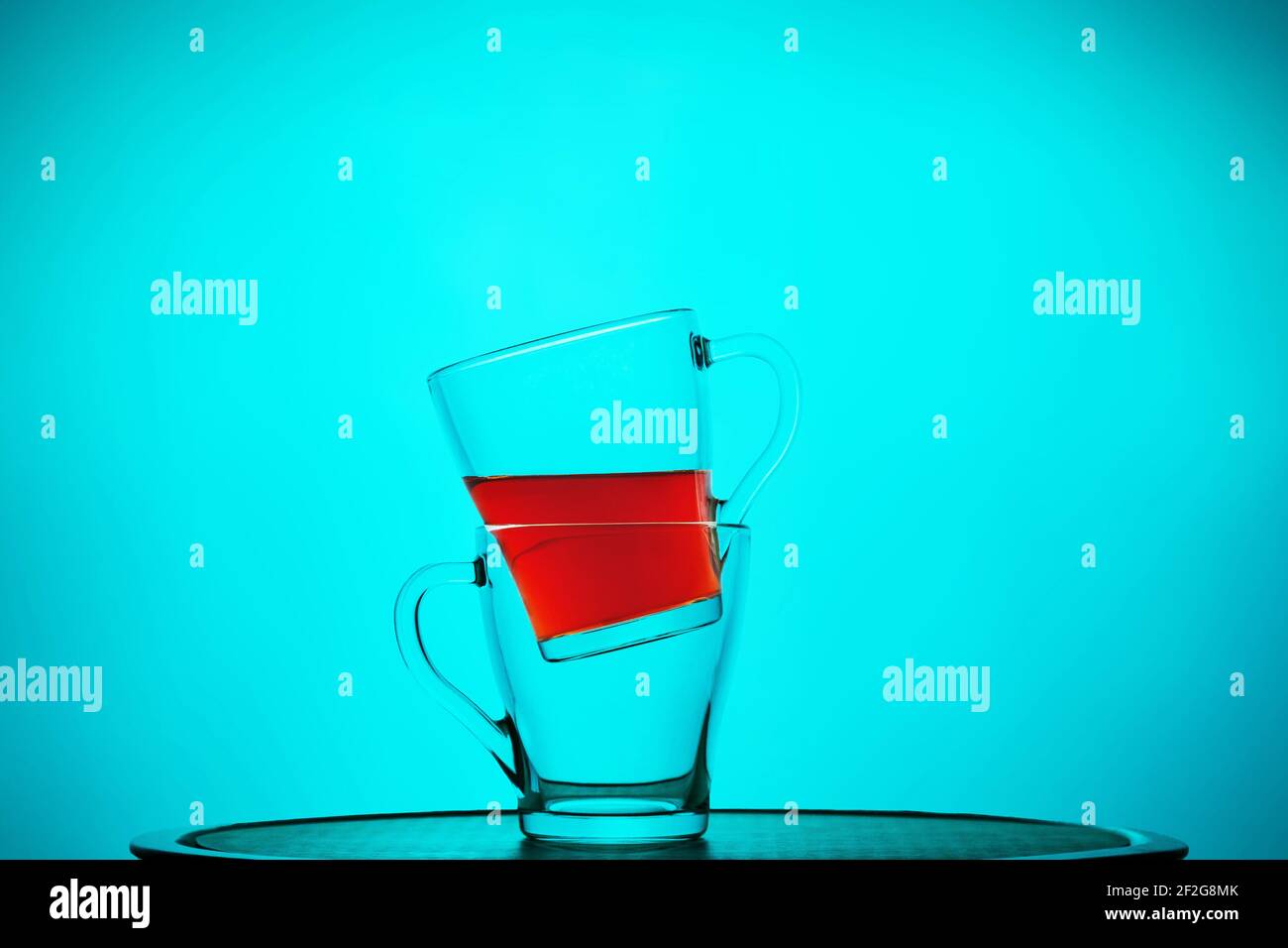 Glass mugs with tea, one inside the other, still life on a blue background. Close-up Stock Photo