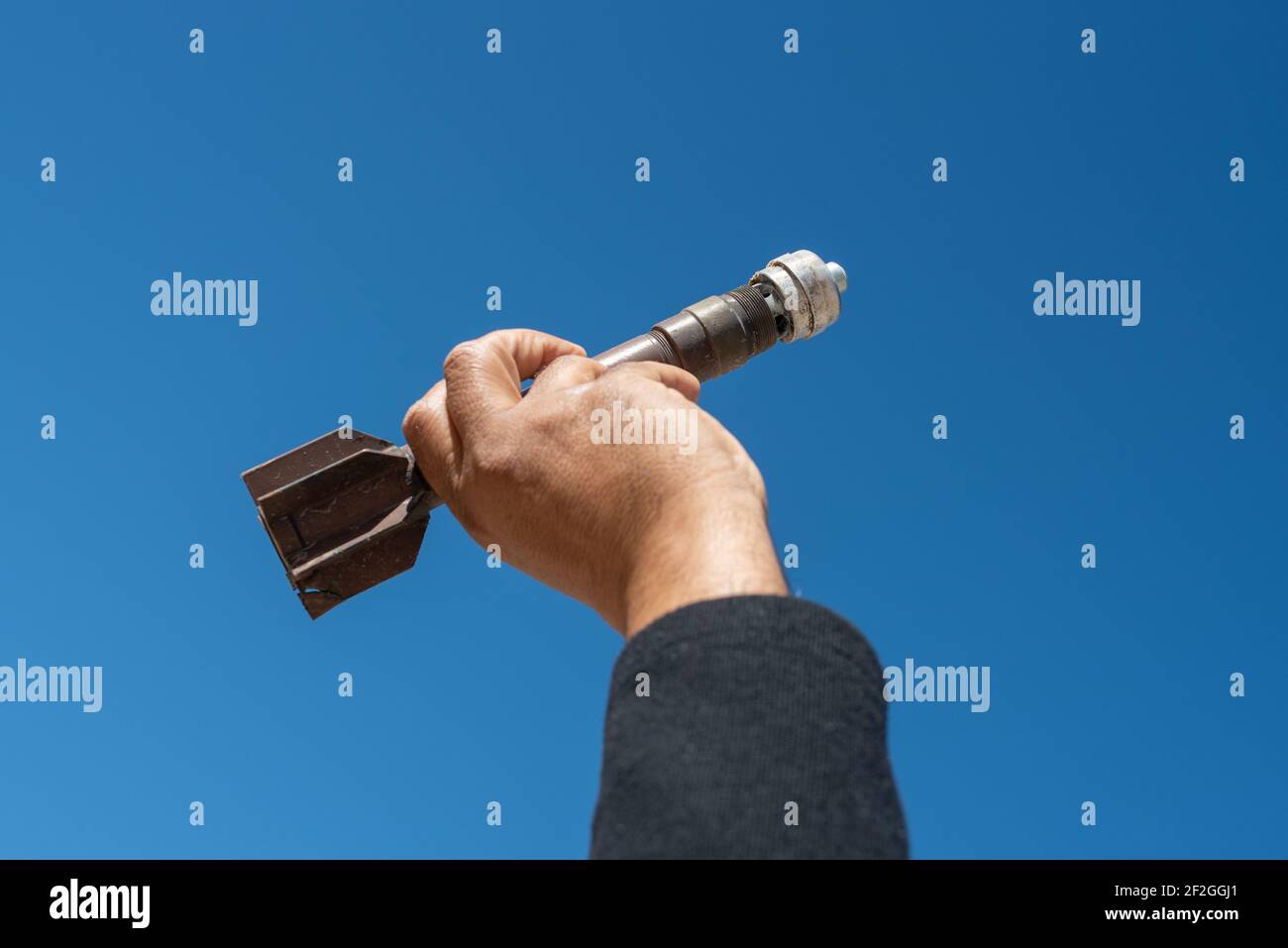 Mortar weapon bomb in man hands on blue sky background. Stock Photo