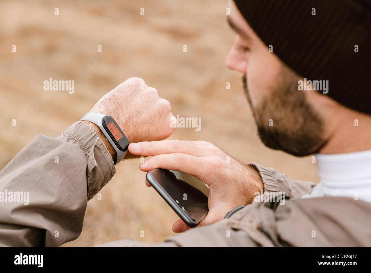 Focused handsome man using smartwatch and cellphone while working out in nature Stock Photo