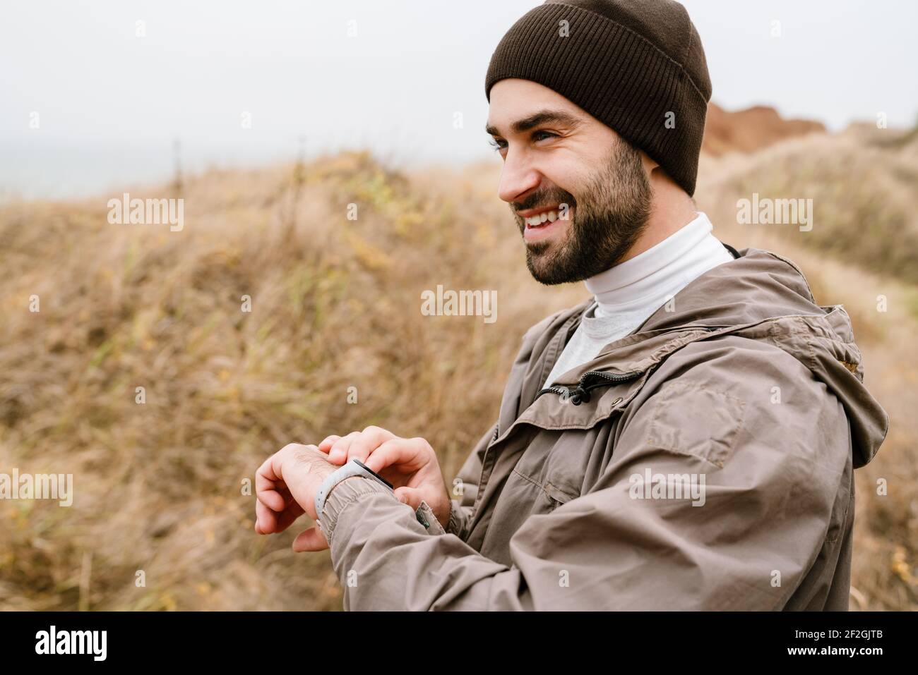 Happy handsome man smiling and using smartwatch while working out in nature Stock Photo