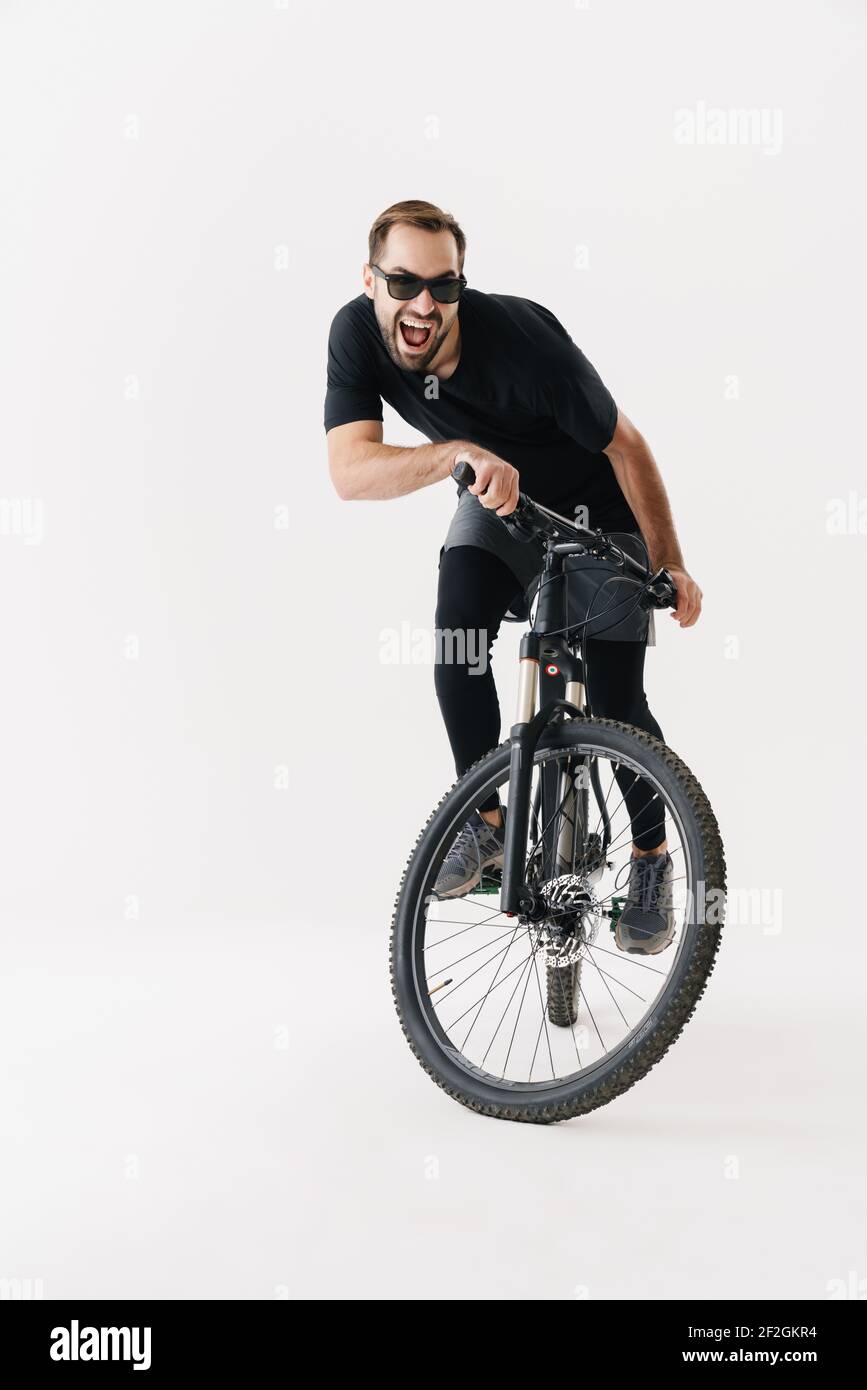 Excited young sportsman in sunglasses riding his bicycle isolated over