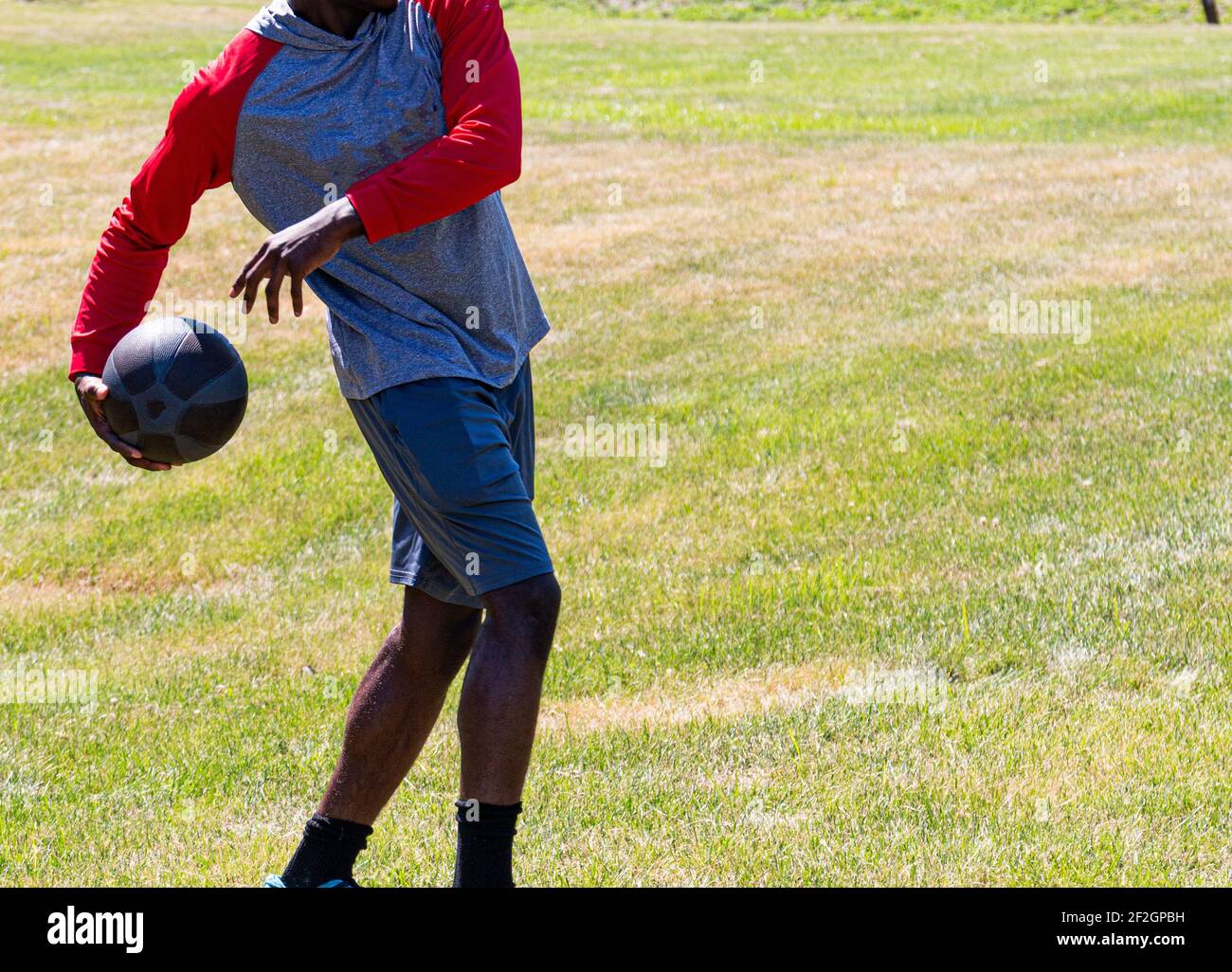 African American male teenager throwing a medicine ball behind his back during track and field practice on grass. Stock Photo