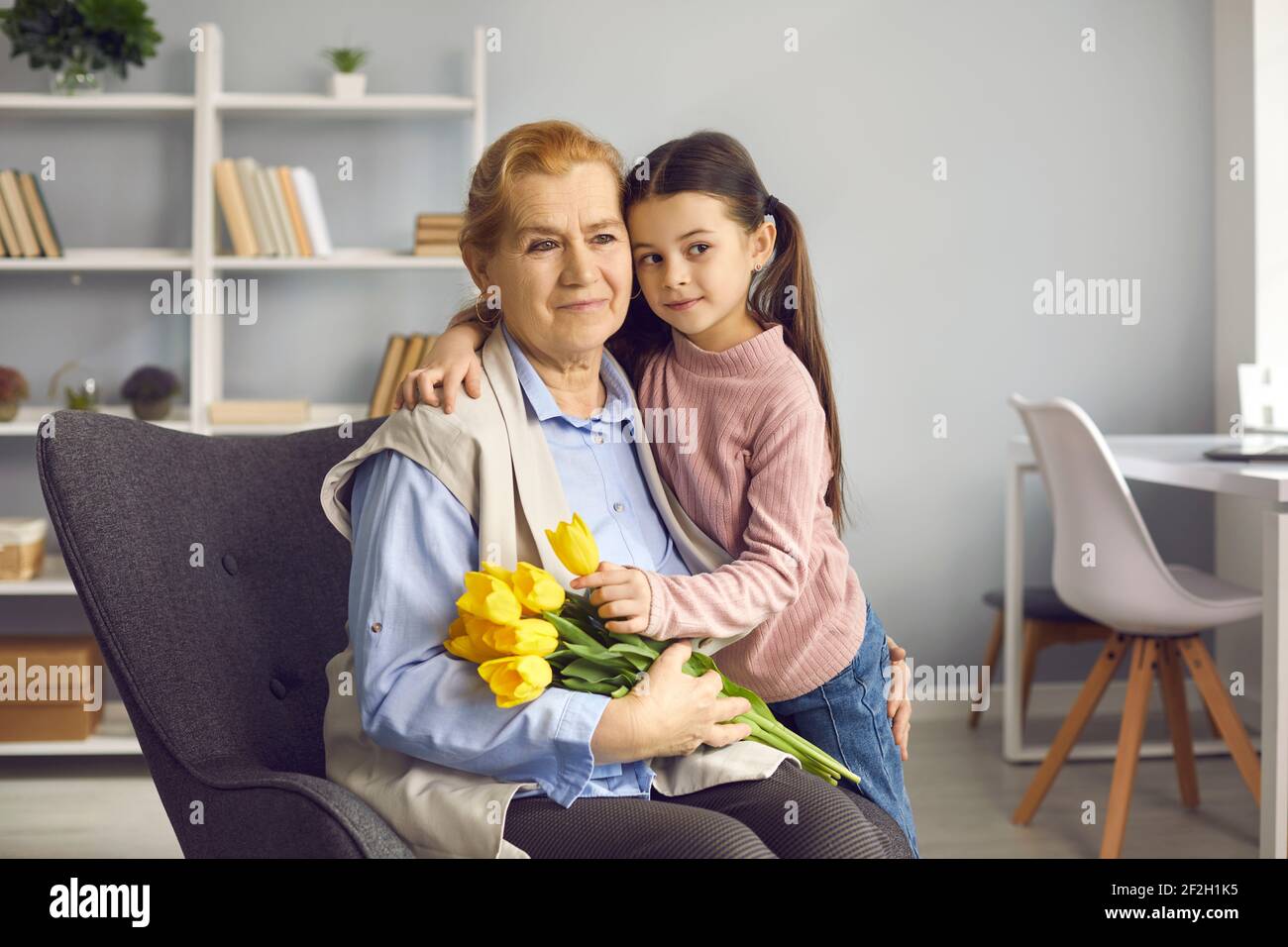 Portrait of a grandmother and little granddaughter with a bouquet of tulips hugging and looking away Stock Photo