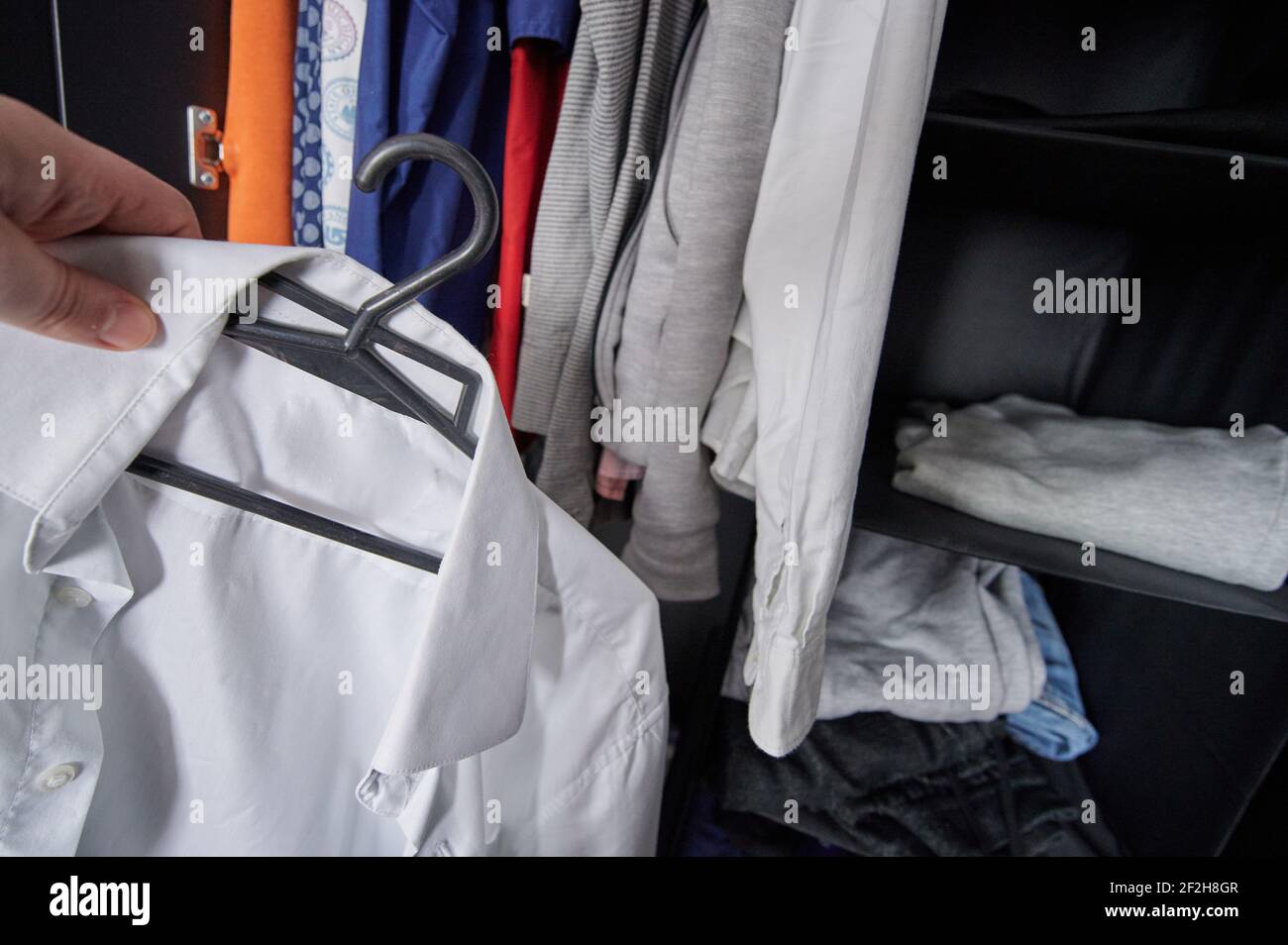 Man take white clean shirt from messy wardrobe Stock Photo