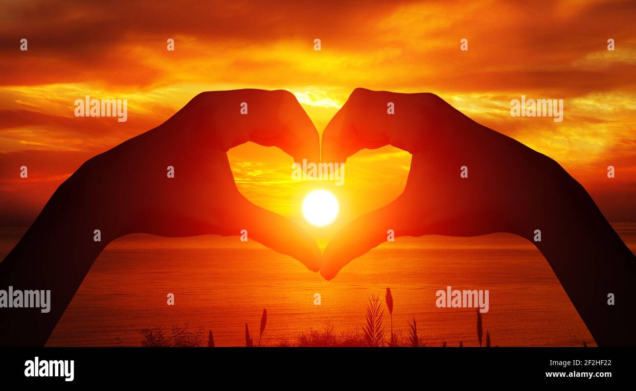 Heart shaped female hands silhouette with sunset background Stock Photo