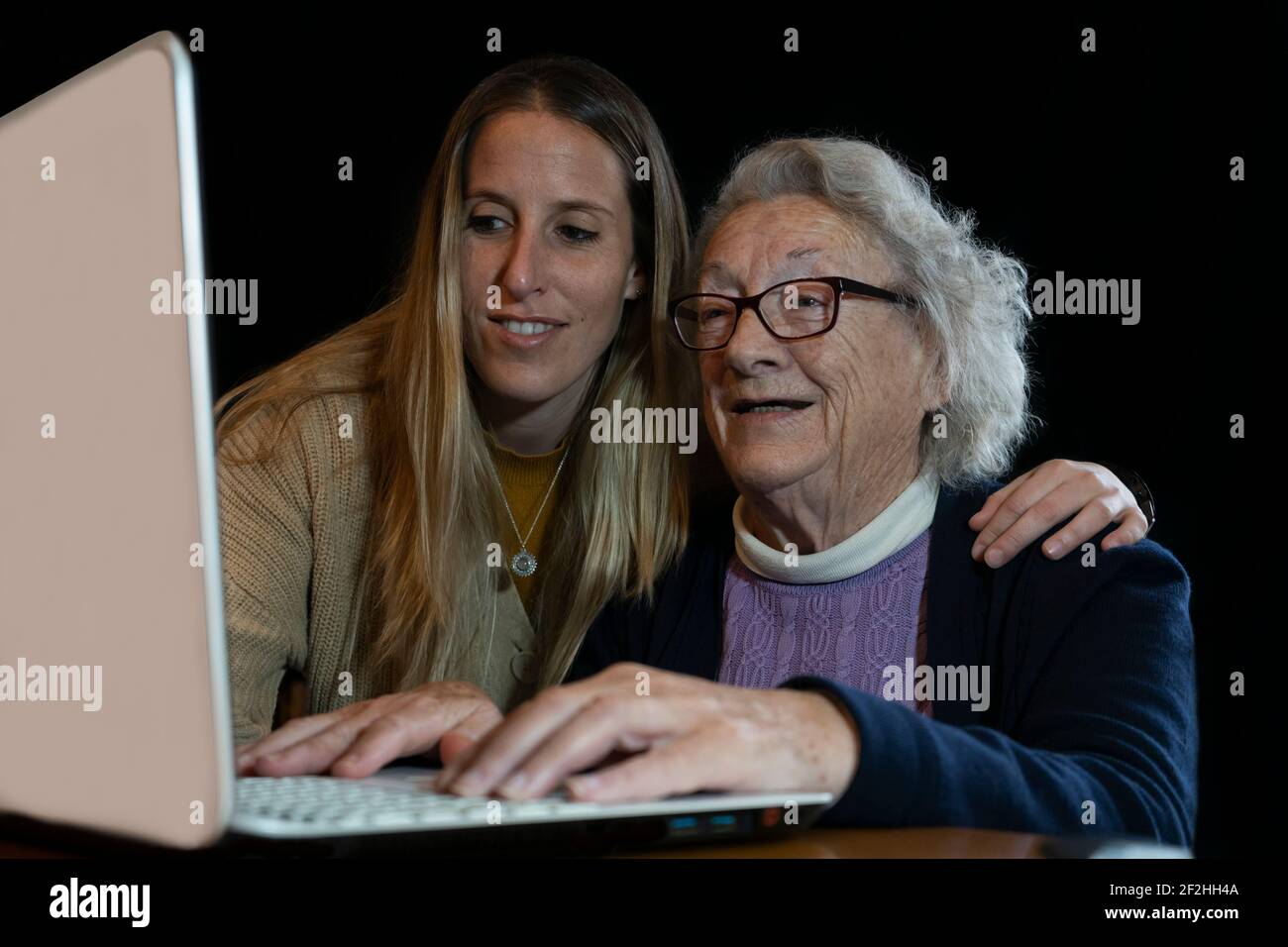 Smiling senior 80s woman with granddaughter using computer.Young female help or teach to surf internet grandparent.Family having fun together watching Stock Photo