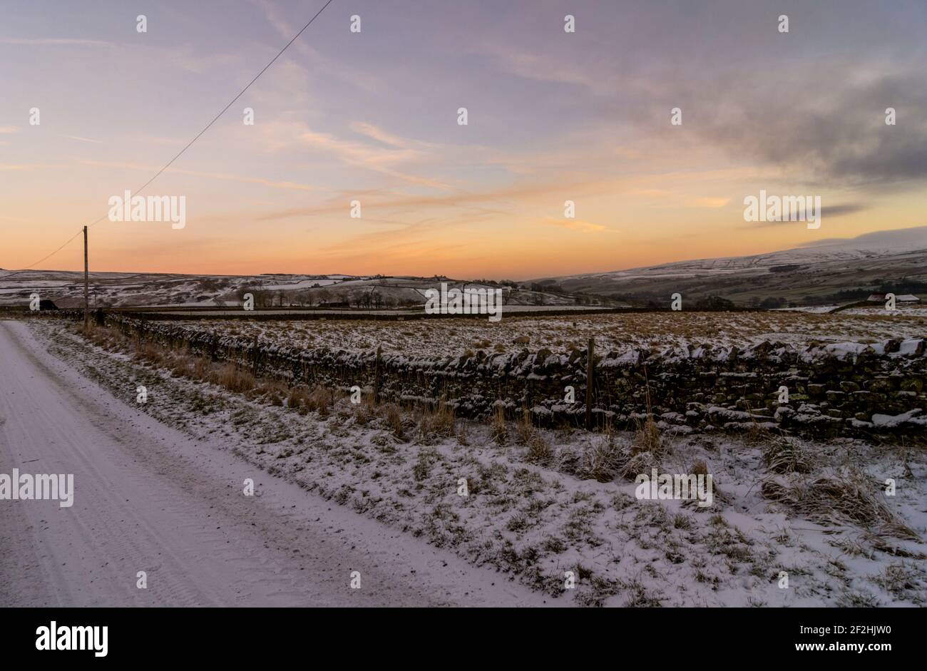 A snow covered country lane at sunset in winter in Weardale, the North Pennines, County Durham, UK Stock Photo