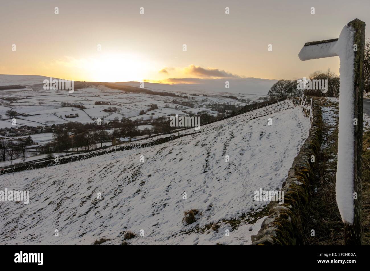 A snow covered Public Footpath sign points across sloping fields at sunset in Weardale, the North Pennines, County Durham, UK Stock Photo