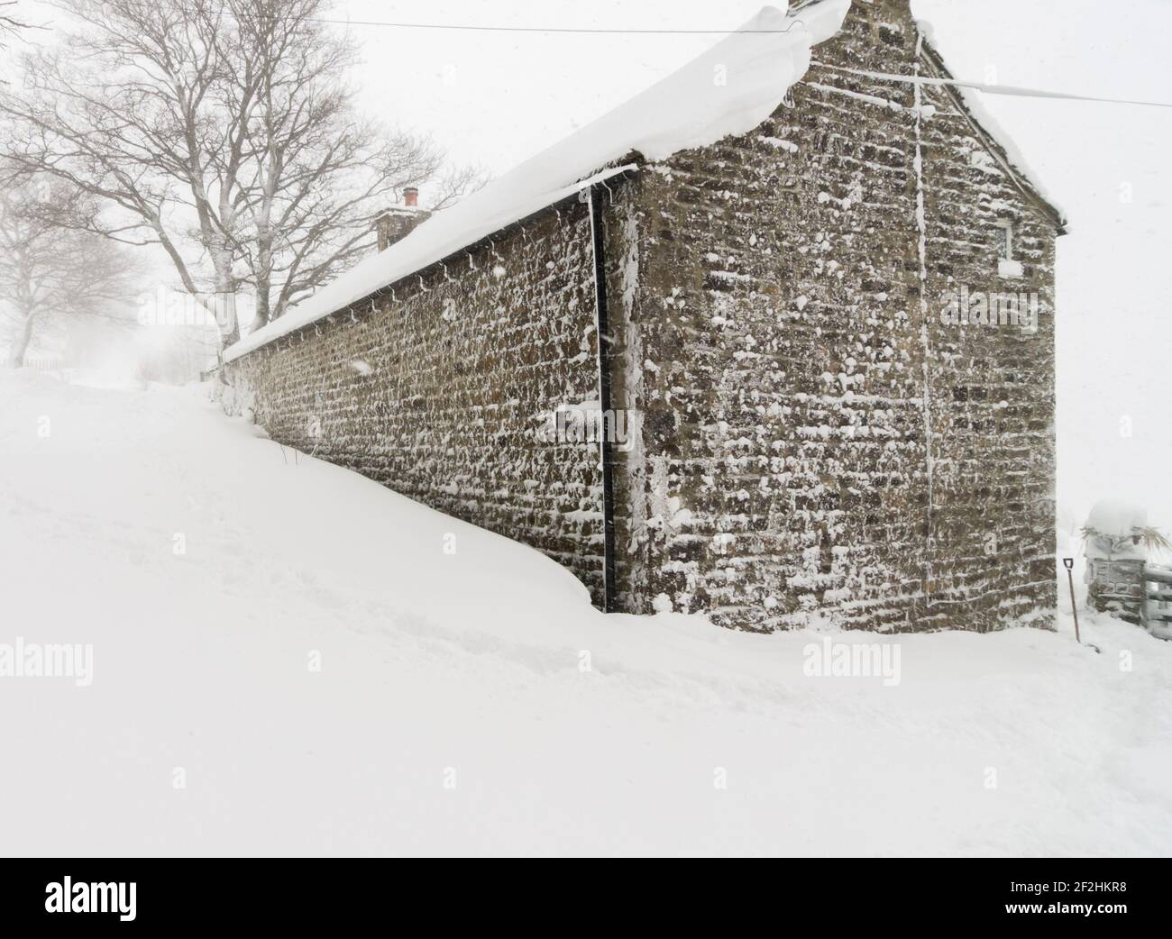 An old stone house built into a steep bank covered in heavy snow in Weardale, the North Pennines, County Durham, UK Stock Photo