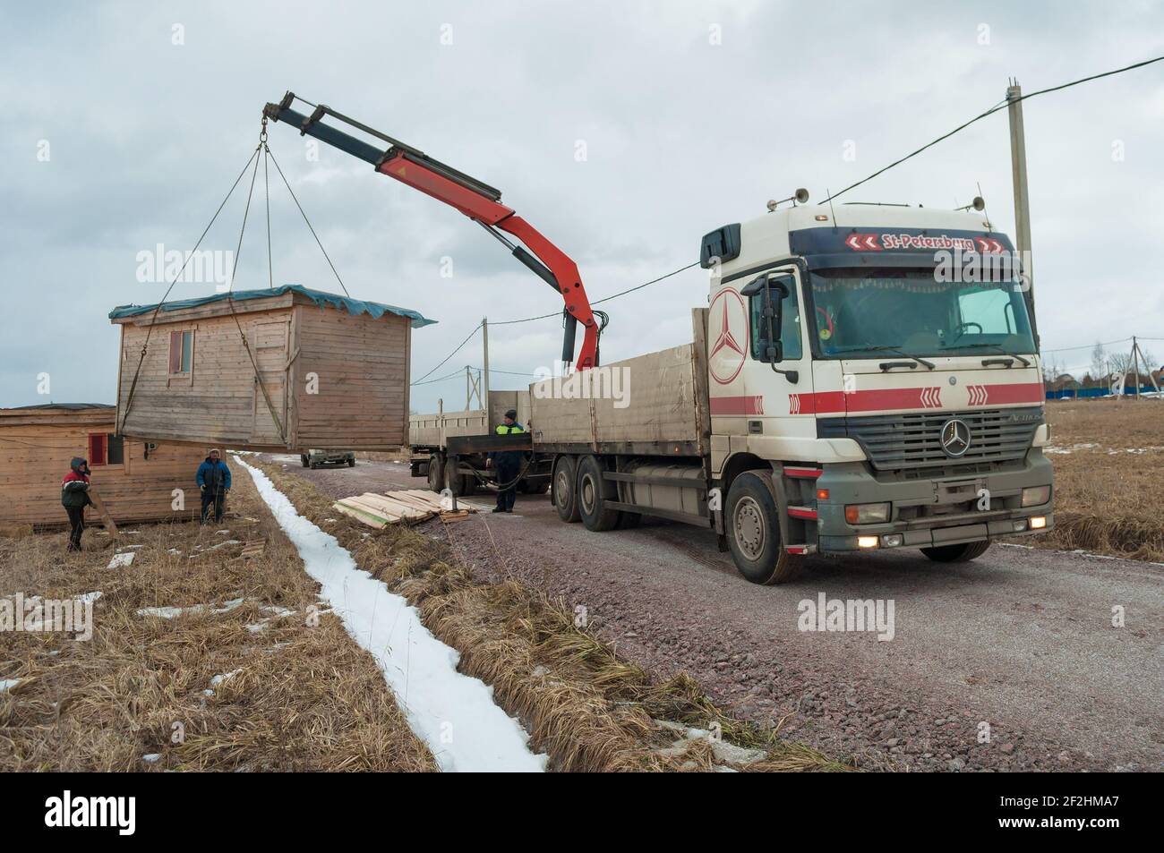 LENINGRAD REGION, RUSSIA - MARCH 04, 2021: Truck with crane manipulator unloads construction house for construction site arrangement Stock Photo