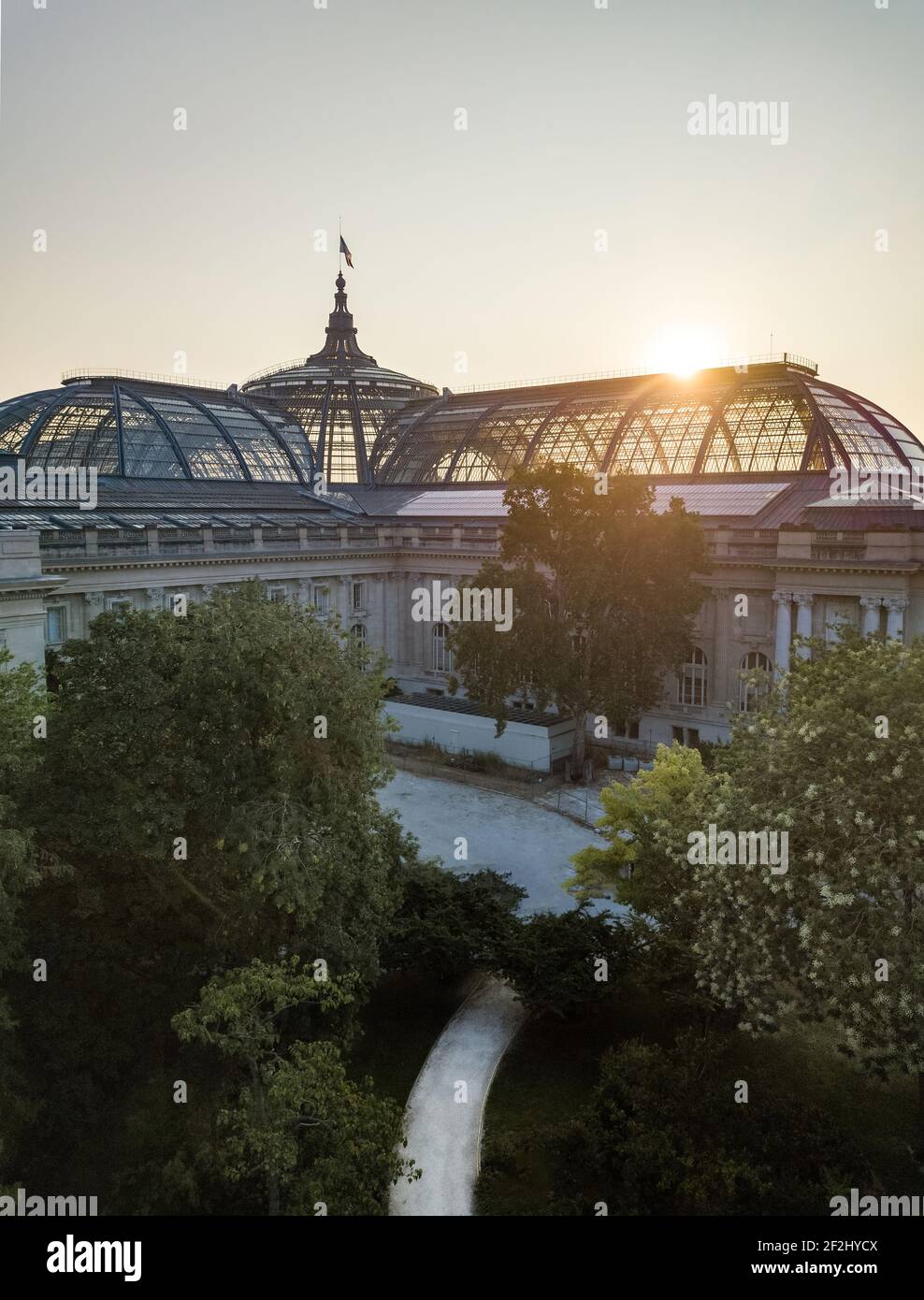 Aerial Sunrise glaring over glass roof and Dome of the Grand Palais of Beaux Arts Architecture (Champs Élysées) in Paris, topped by the French flag Stock Photo
