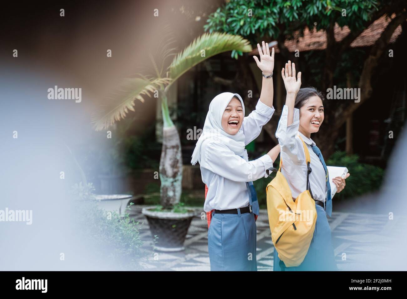 view of a shot from above the back of a high school student with two female high school students wearing school bags waving Stock Photo
