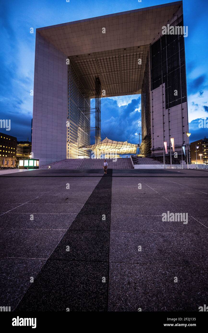 Tourist standing in front of La Grande Arche de la Défense against cloudy sky from concrete floor In financial district in the west of Paris, France Stock Photo