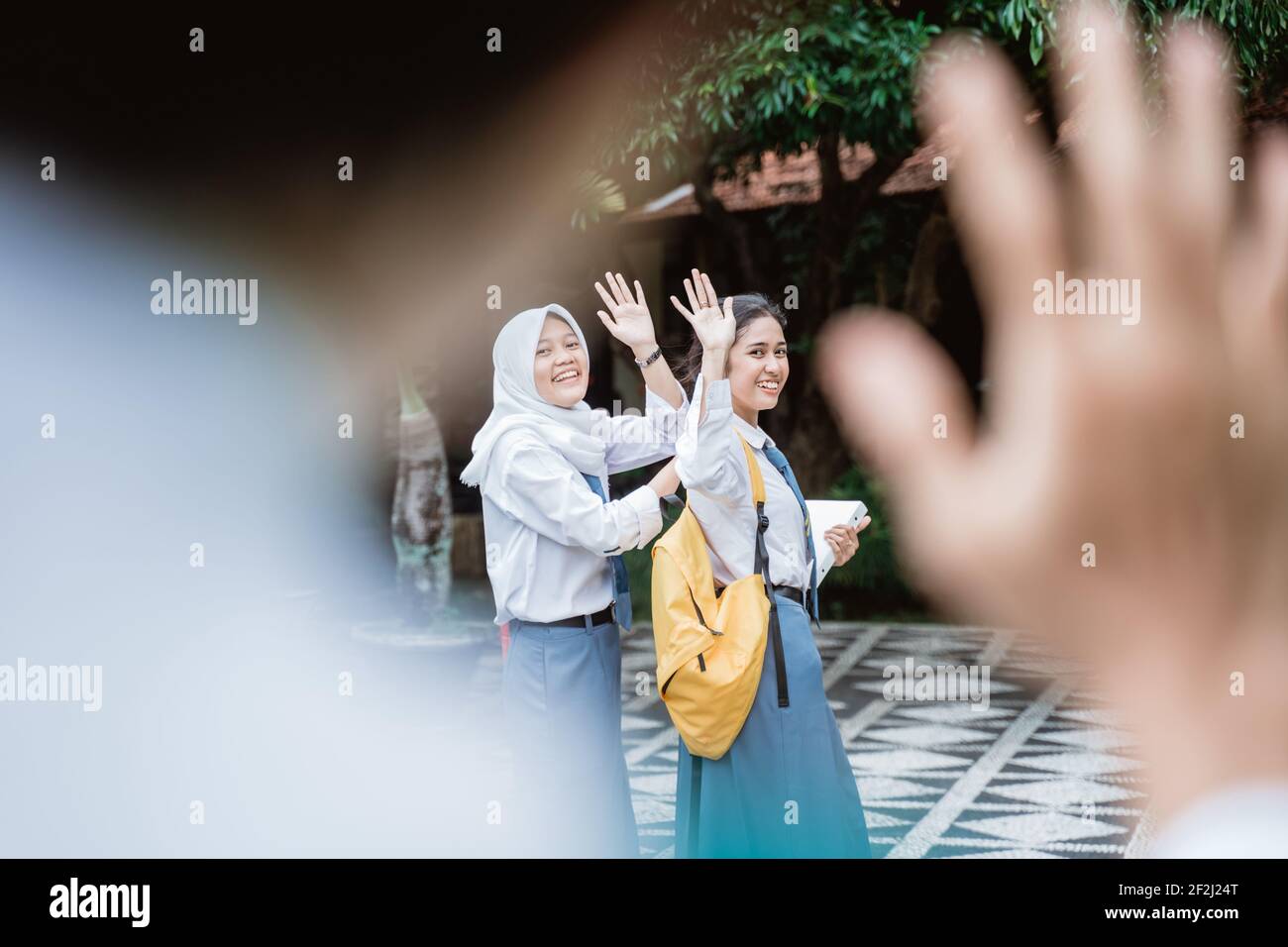 view of shot from beside the waving hand a high school student with two female high school students wearing a school bag waving Stock Photo