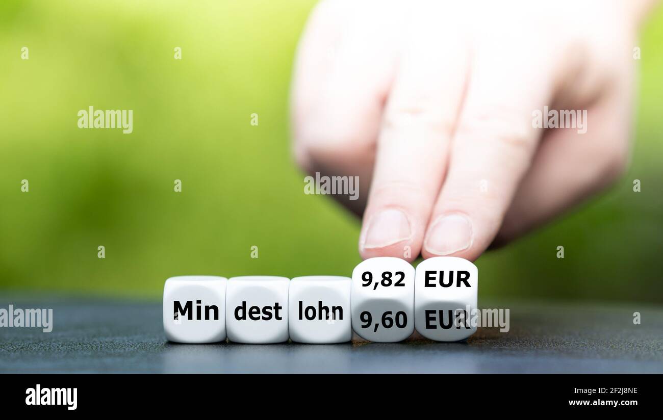 Hand turns dice and changes the German expression 'Mindestlohn 9,60 EUR' (minimum wage 9,60 EUR) to 'Mindestlohn 9,82 EUR' (minimum wage 9,82 EUR). Stock Photo