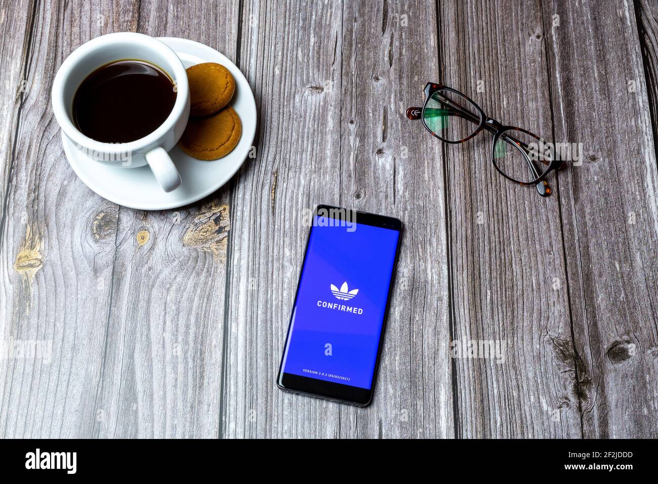 A Mobile phone or cell phone laid on a wooden table with the Adidas Confirmed app open on screen Stock Photo