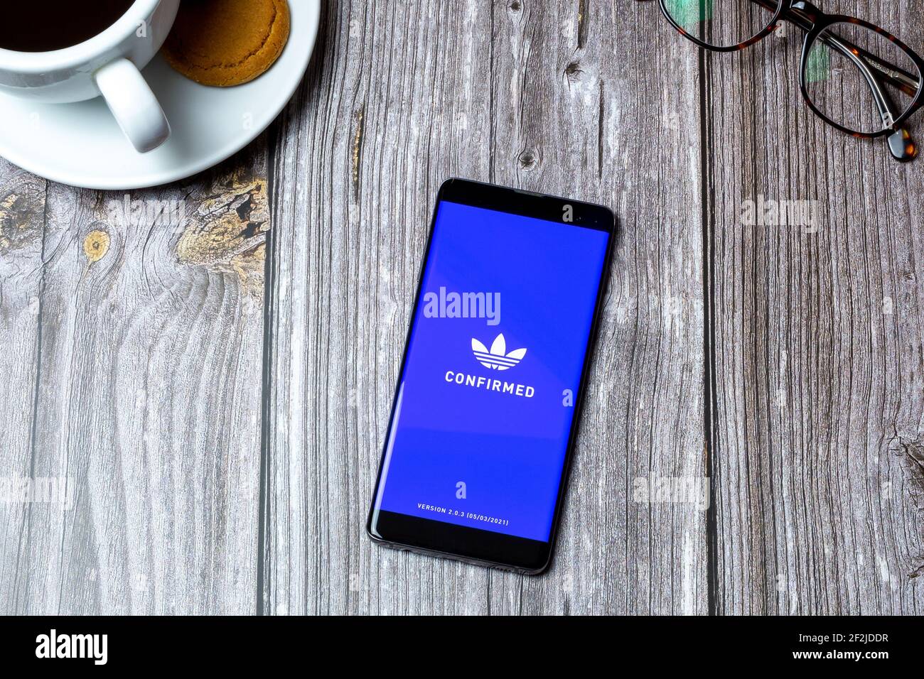 A Mobile phone or cell phone laid on a wooden table with the Adidas Confirmed app open on screen Stock Photo