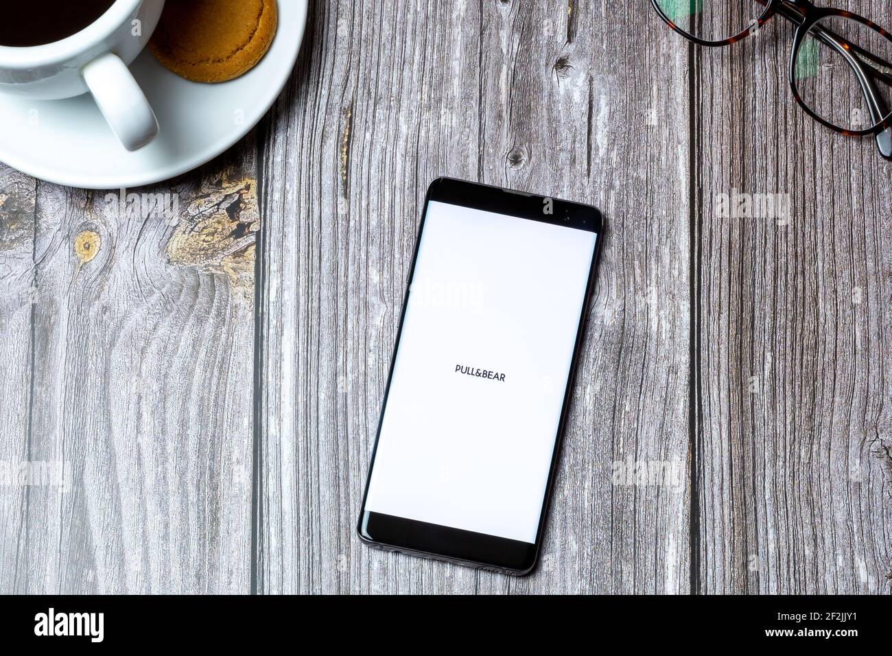 A Mobile phone or cell phone laid on a wooden table with the Pull & Bear app open on screen Stock Photo