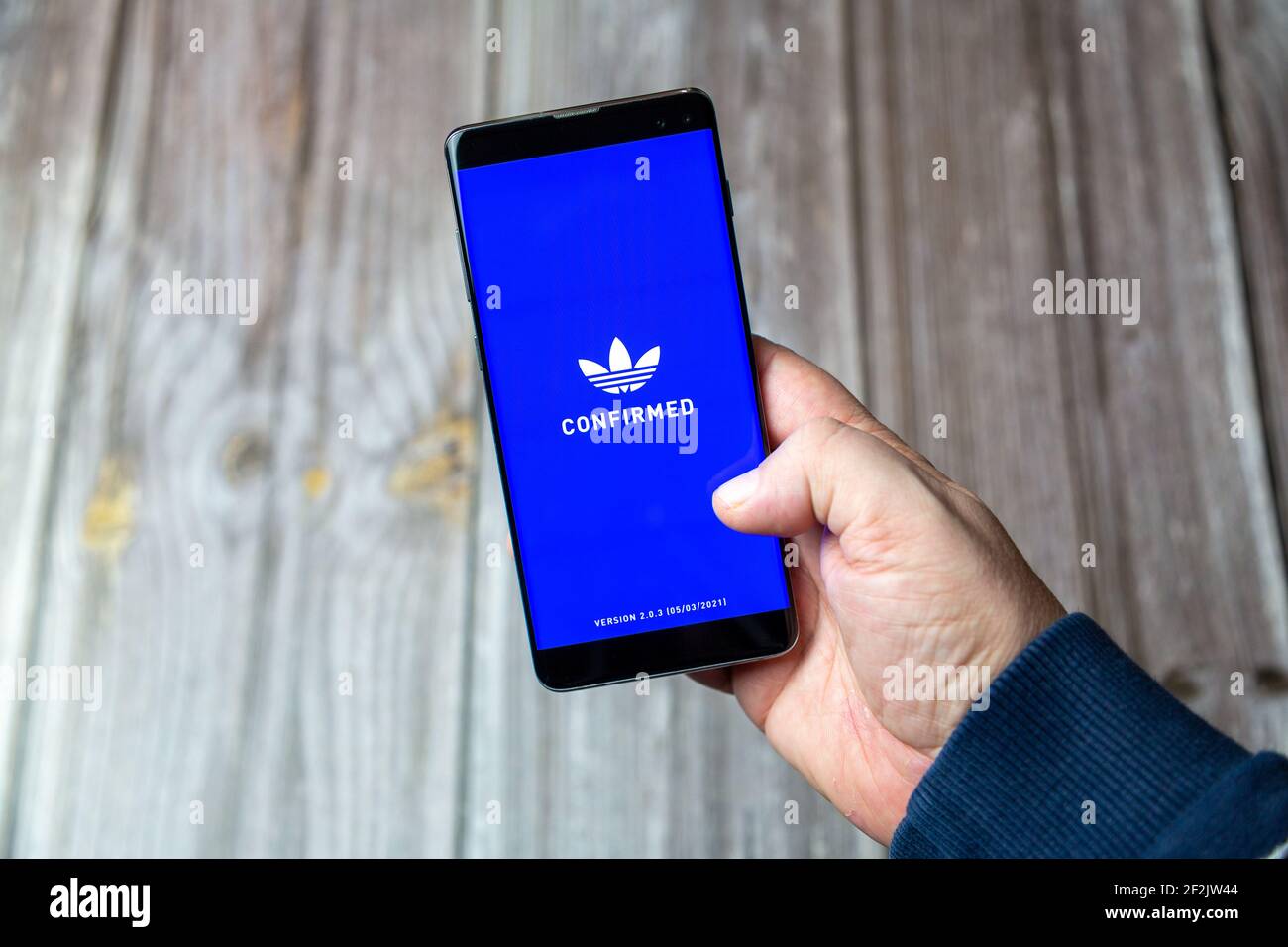 A Mobile phone or cell phone being held in a hand with the Adidas Confirmed app open on screen Stock Photo