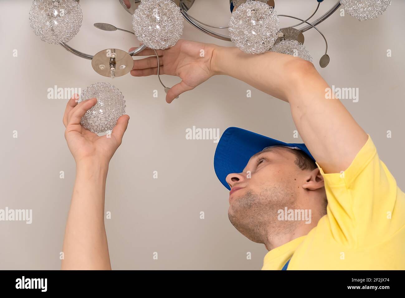 Electrician screws the ceiling light from the chandelier on the stretch ceiling close-up Stock Photo