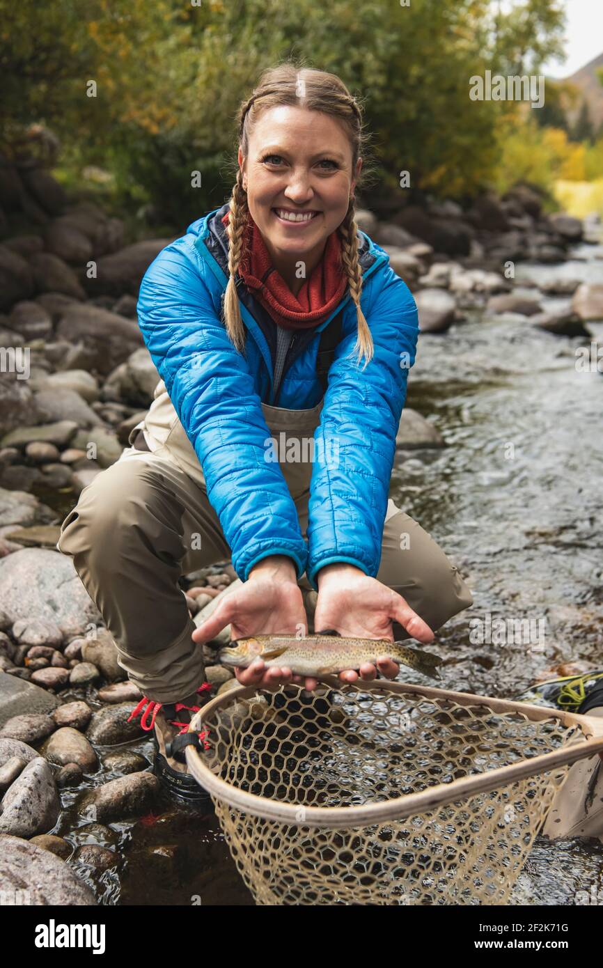 Portrait of smiling young woman with fish catch at stream in forest Stock Photo