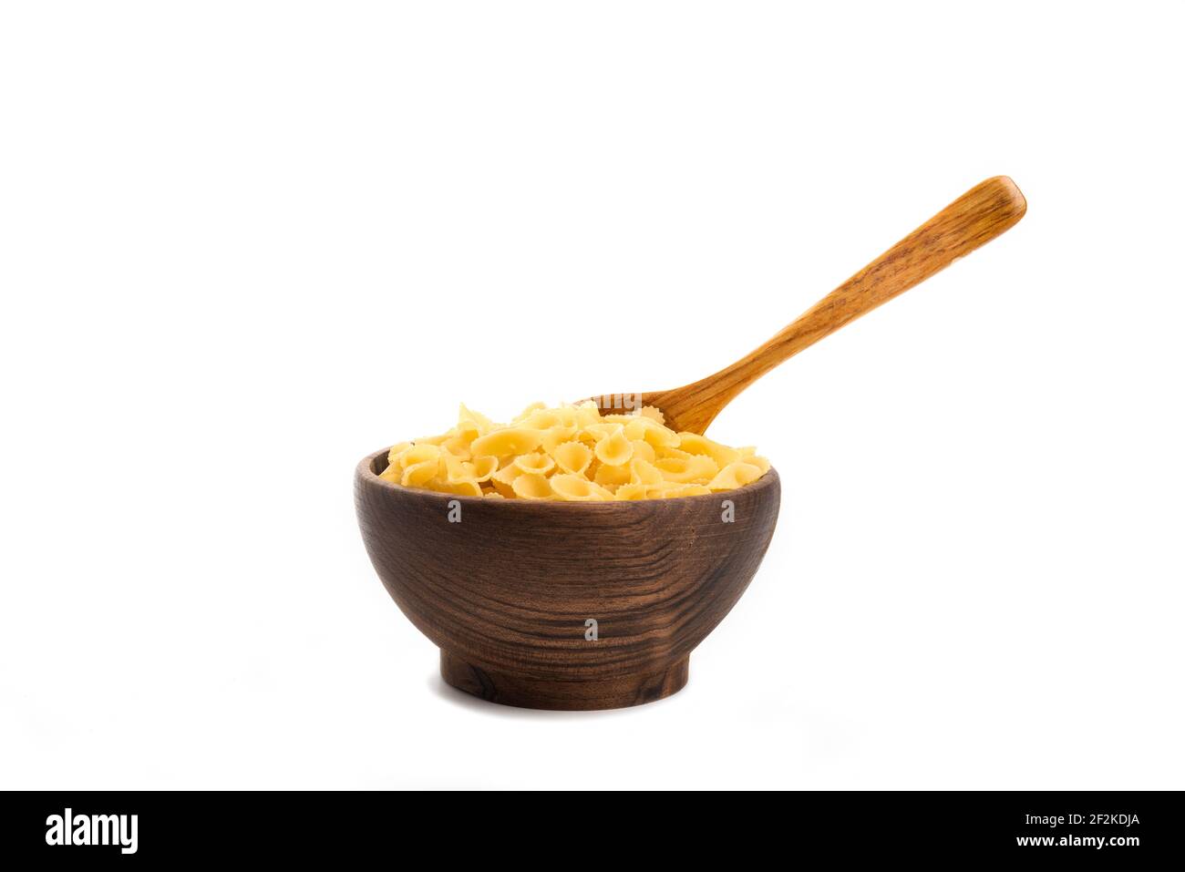 A wooden bowl full of dry uncooked whole wheat Italian pasta with wooden spoon Stock Photo