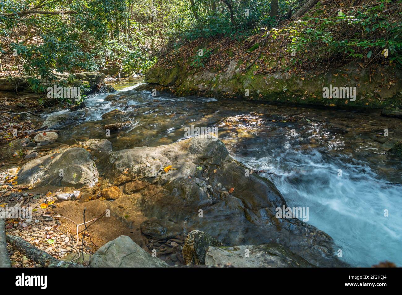 Fast moving water through the rocks and boulders going downstream in the forest in the north Georgia mountains on a sunny day in autumn Stock Photo