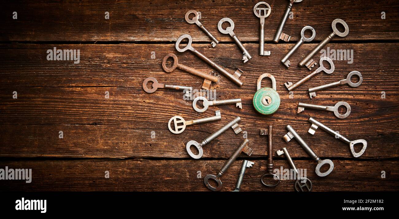 Vintage rusty padlock surrounded by group of old keys on a weathered wooden background. Internet security and data protection concept, blockchain and Stock Photo