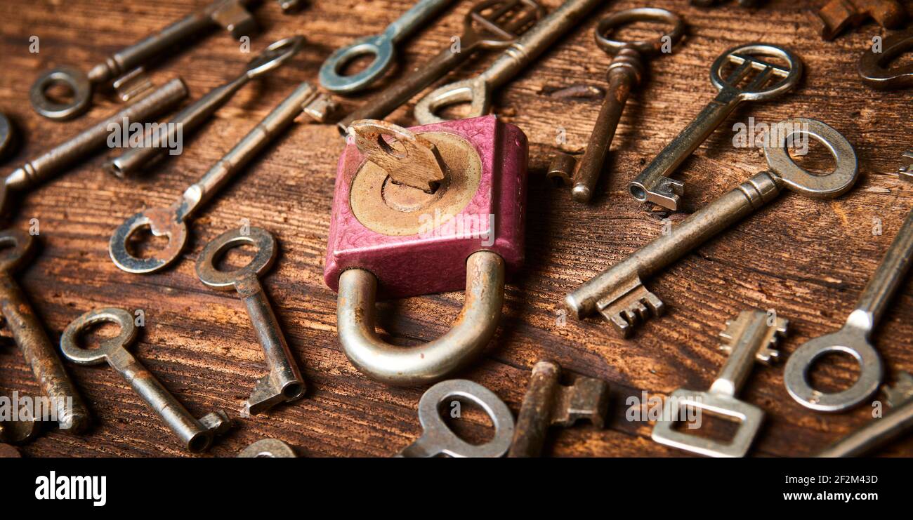 Vintage rusty padlock surrounded by group of old keys on a weathered wooden background. Internet security and data protection concept, blockchain and Stock Photo