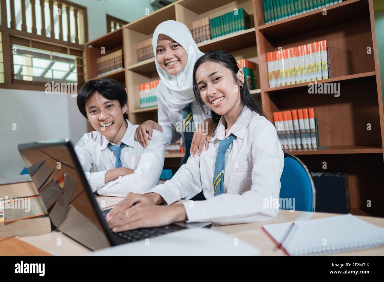three Asian high school students smile into the camera while studying ...