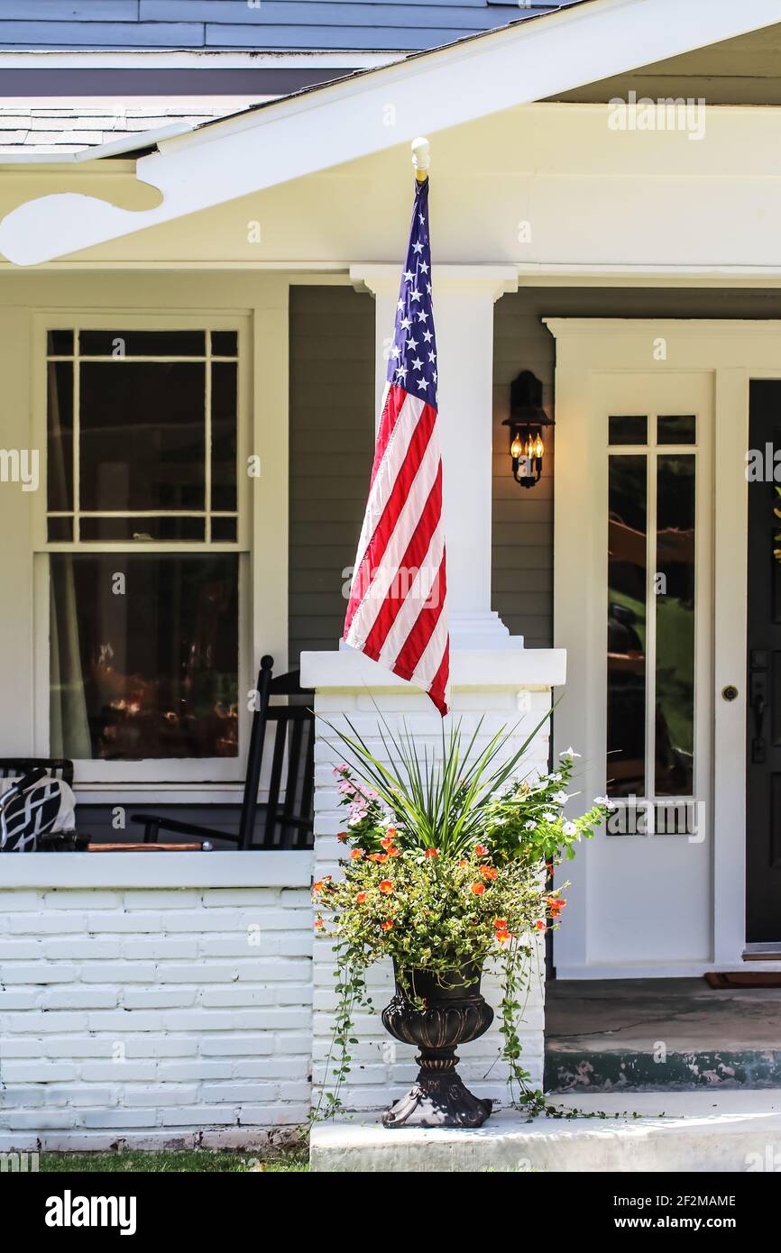 Closeup of entrance to cottage house with beautiful flowers in a pot and American flag by porch Stock Photo