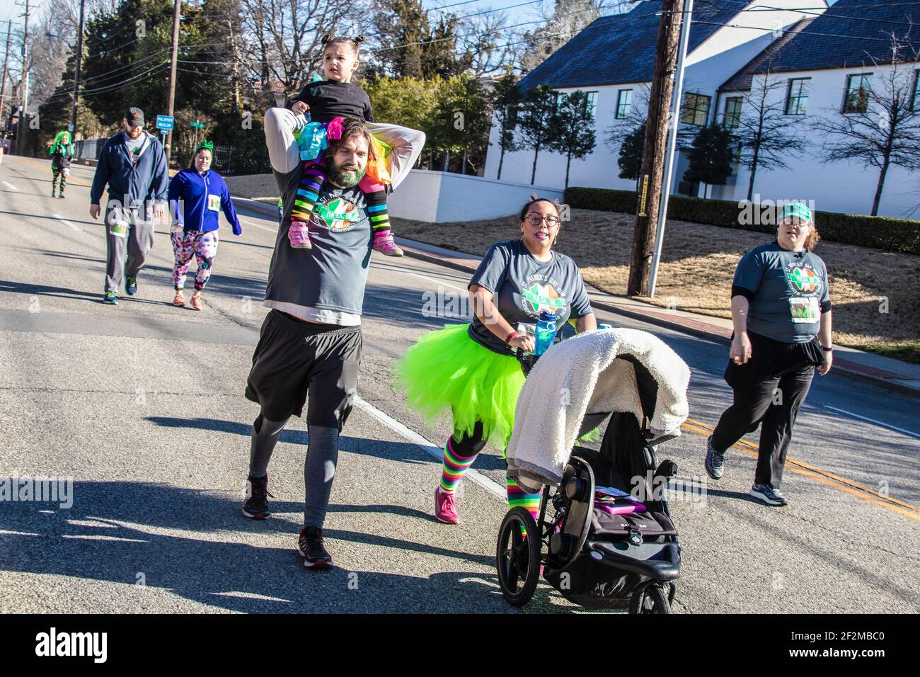 3-16-2019 Tulsa USA -Couple in St Patricks Day Tee shirts and costumes walk in a charity run - she pushes baby carriage and he carries little girl on Stock Photo