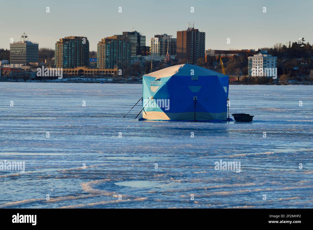 Blue ice fishing tent on frozen Kempenfelt Bay of Lake Simcoe in winter with downtown Barrie condos at sunset Stock Photo