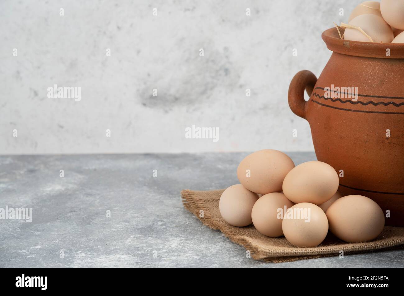 Clay pot full of raw chicken eggs on marble background Stock Photo
