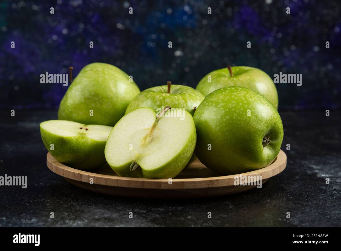 Whole and sliced ripe green apples on wooden plate Stock Photo