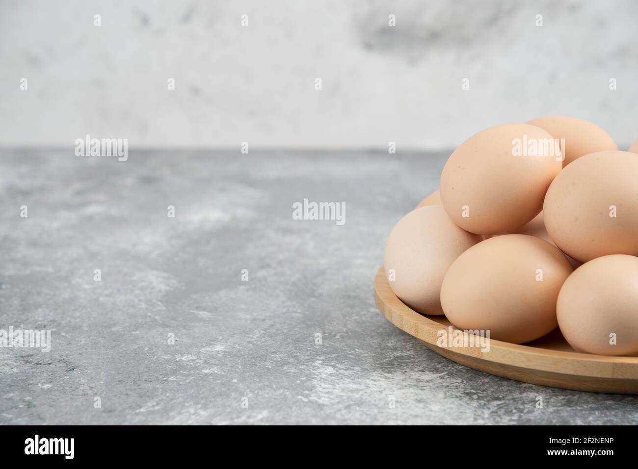 Wooden plate of fresh organic raw eggs on marble surface Stock Photo