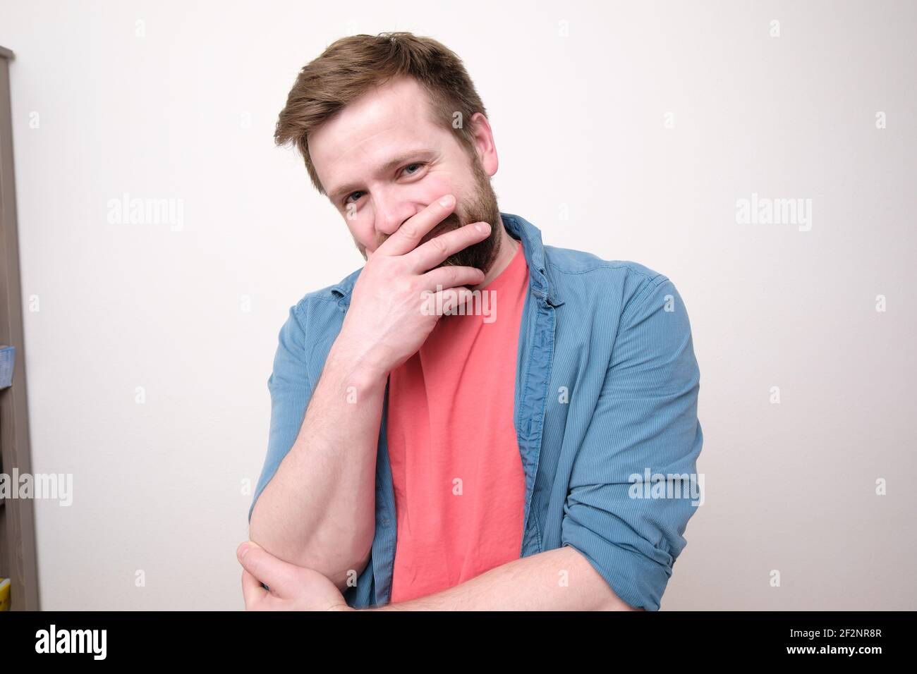 Shy, happy man smiles while covering his mouth with his hand. White background. Stock Photo