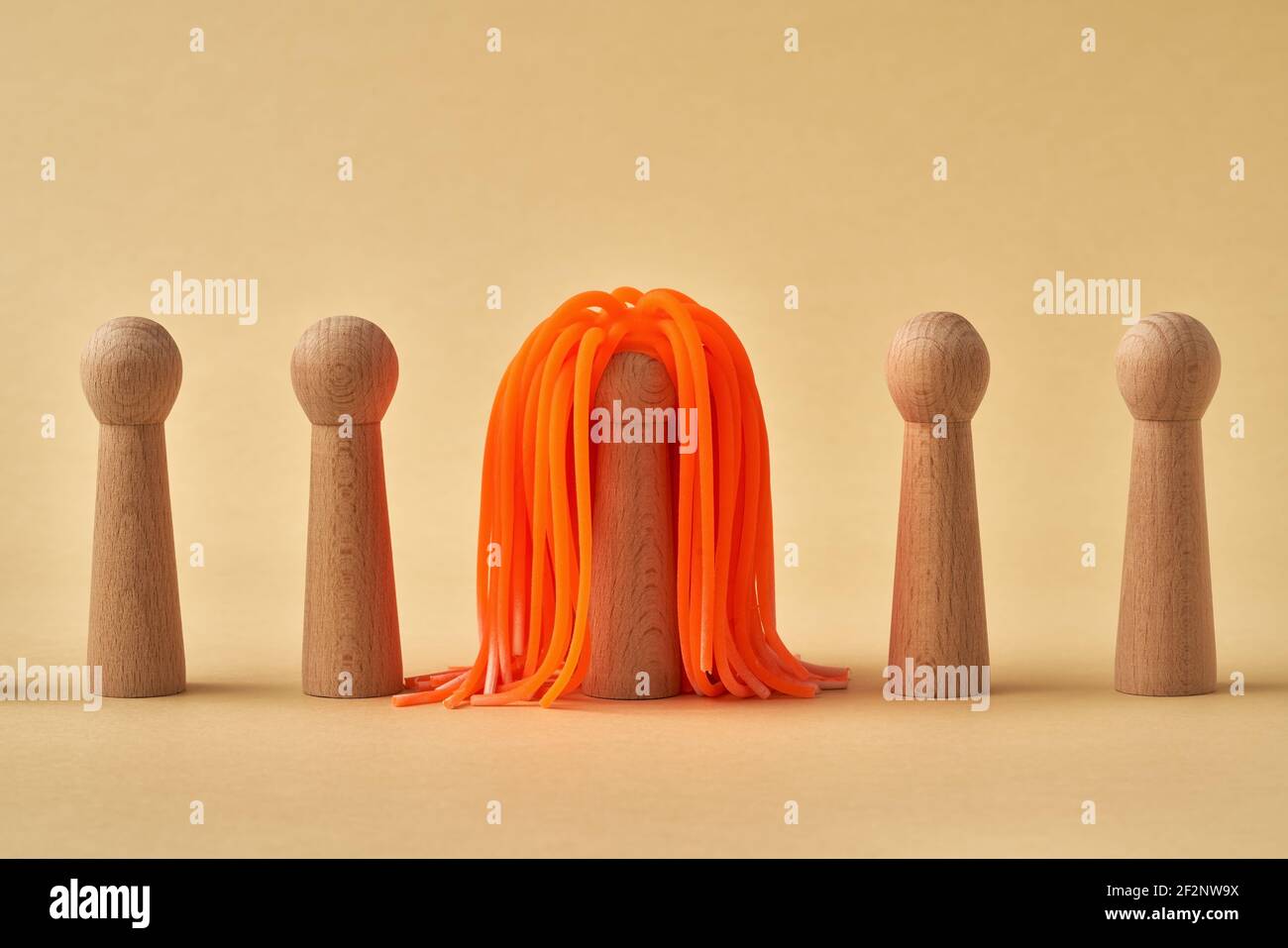 Wooden figures standing in a row, one with striking orange hair Stock Photo