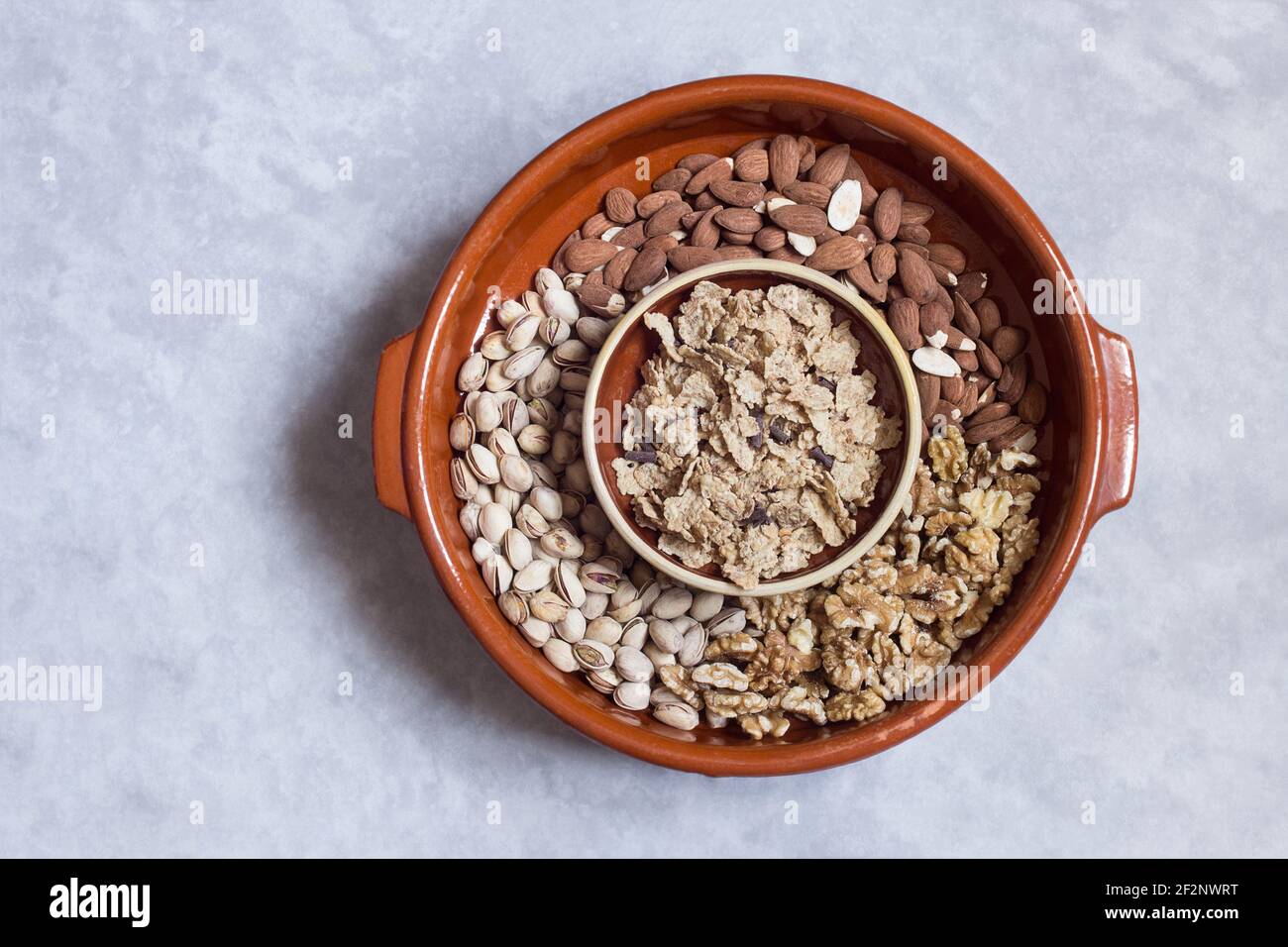 An old earthenware pot filled with mixed dried fruits with a clay bowl filled with toasted rice, whole wheat, and barley flakes with chocolate. Stock Photo