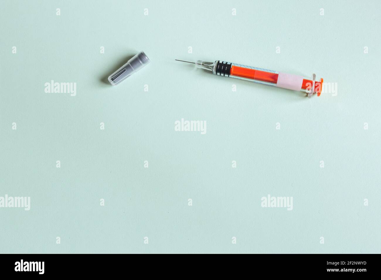 A used vaccination syringe with the needle cap uncapped and no medical solution on a textured green paper background with space to input a text. Stock Photo