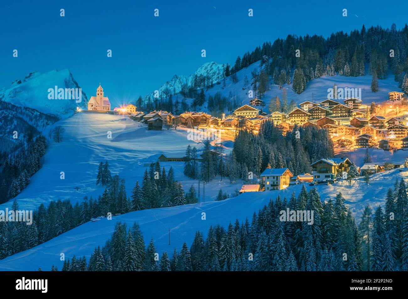 Italy, Veneto, Belluno, Agordino, alpine village of Colle Santa Lucia in winter at dawn, illuminated houses and church, Dolomites Stock Photo