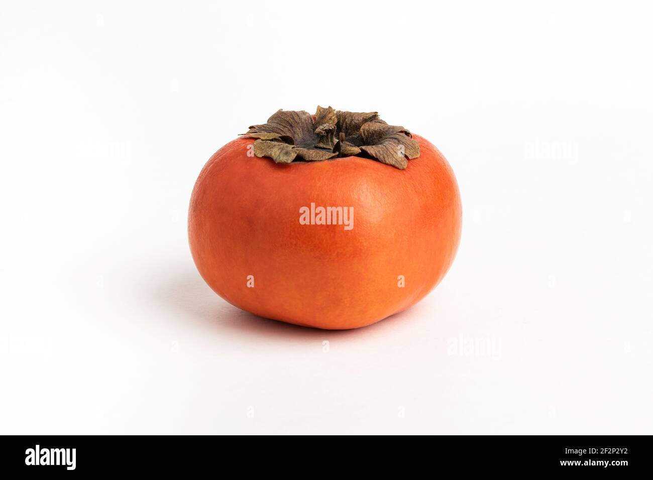 Close-up shot with shallow depth of field of a ripe persimmon fruit set on a plain white background. Stock Photo