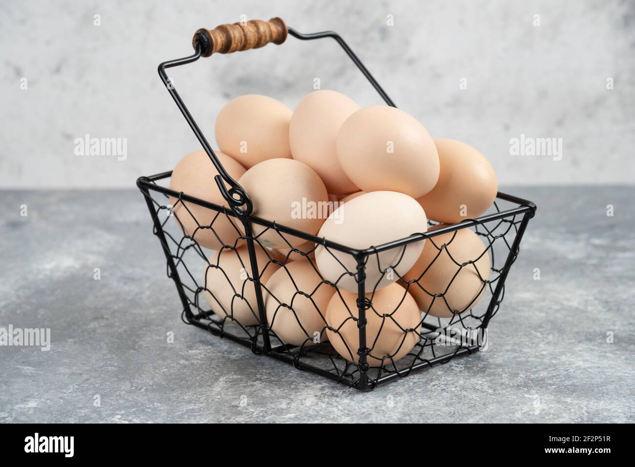 Metal basket of organic fresh uncooked eggs placed on marble surface Stock Photo
