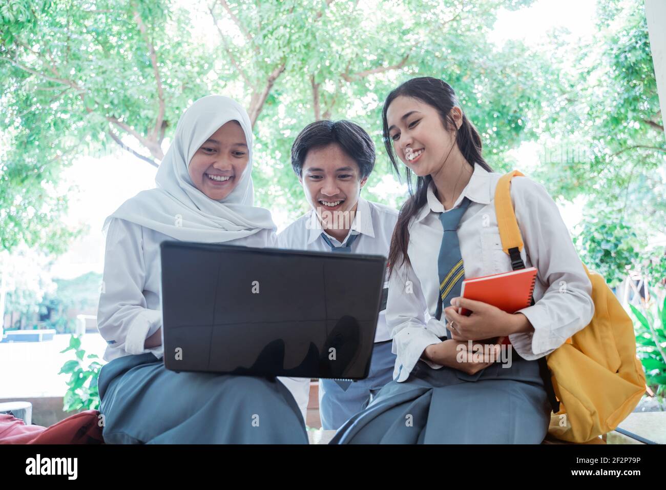 front view of high school students standing with a laptop computer, carrying books, and wearing a bag Stock Photo